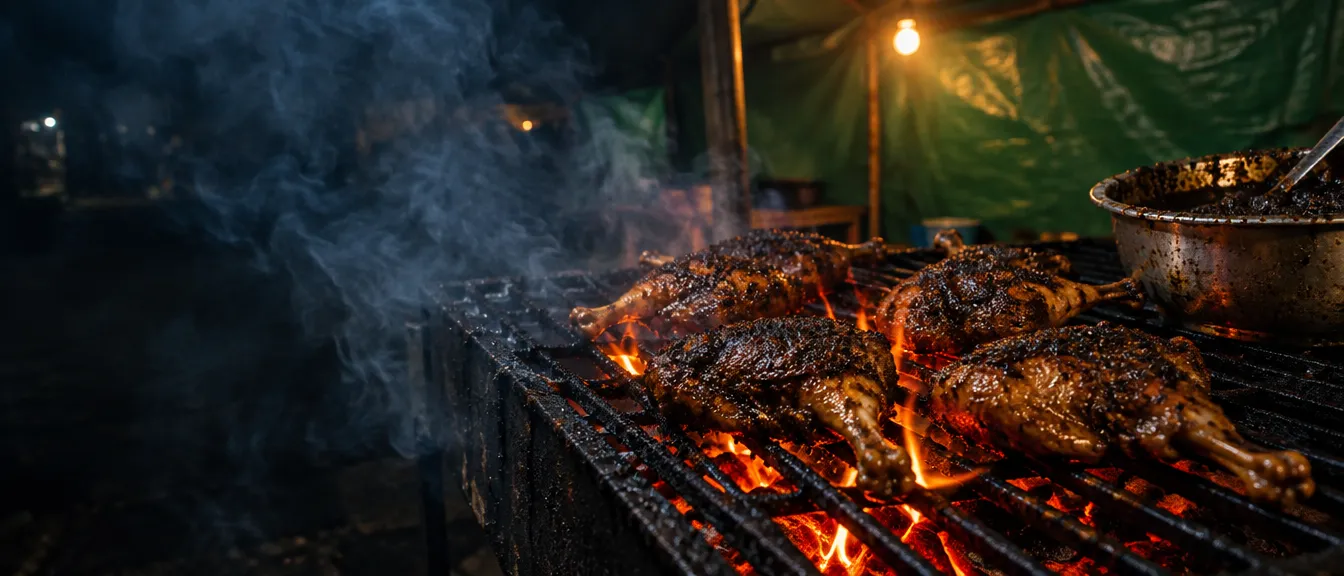Empat potong bebek berlumur bumbu hitam di atas panggangan besi, api kecil menyambar dari lemak yang menetes, tenda terpal hijau di belakang.